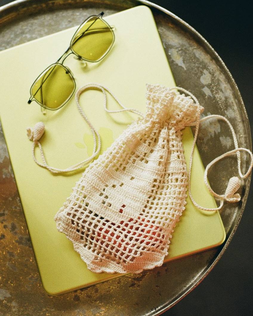 A white handmade Pear pouch styled with sunglasses on a metal tray