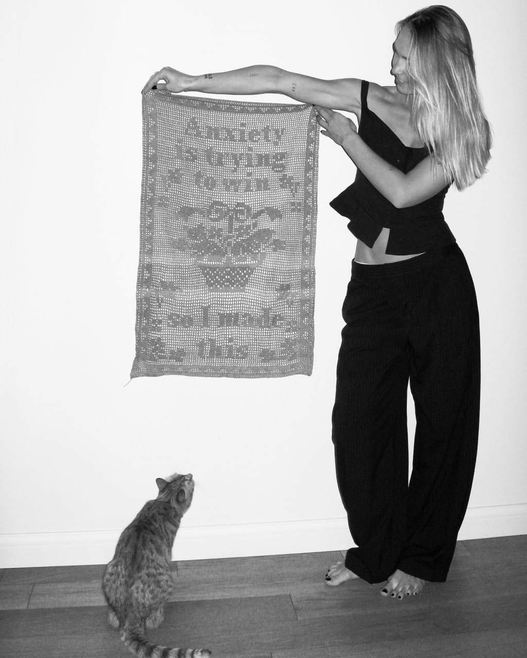 A woman holding a handmade filet-crochet wall hanging beside a cat